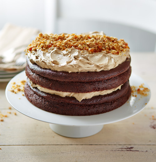 Large salted caramel cake topped with peanut brittle on a white cake stand