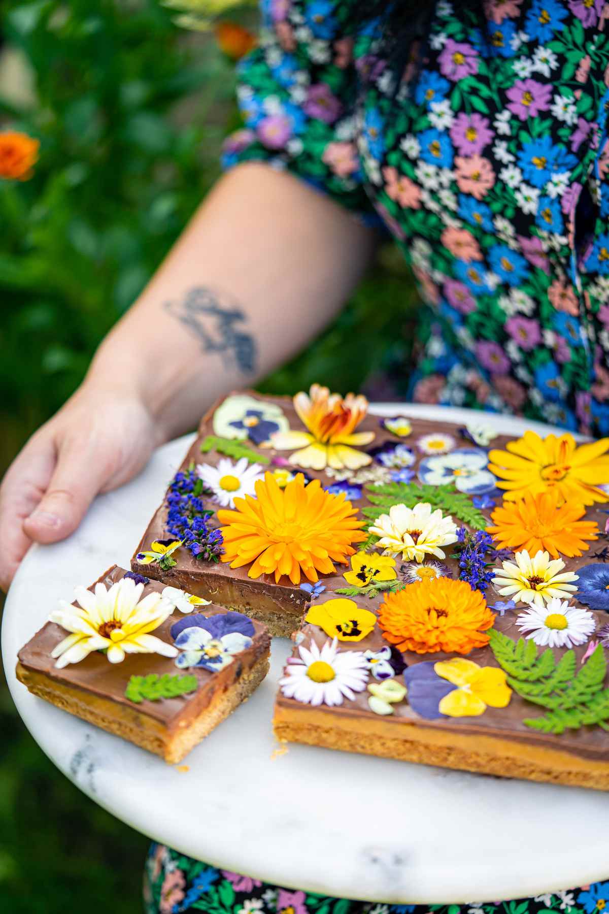 A woman holding a plate of date and pecan millionaire's shortbread. They have an assortment of flowers on the top.