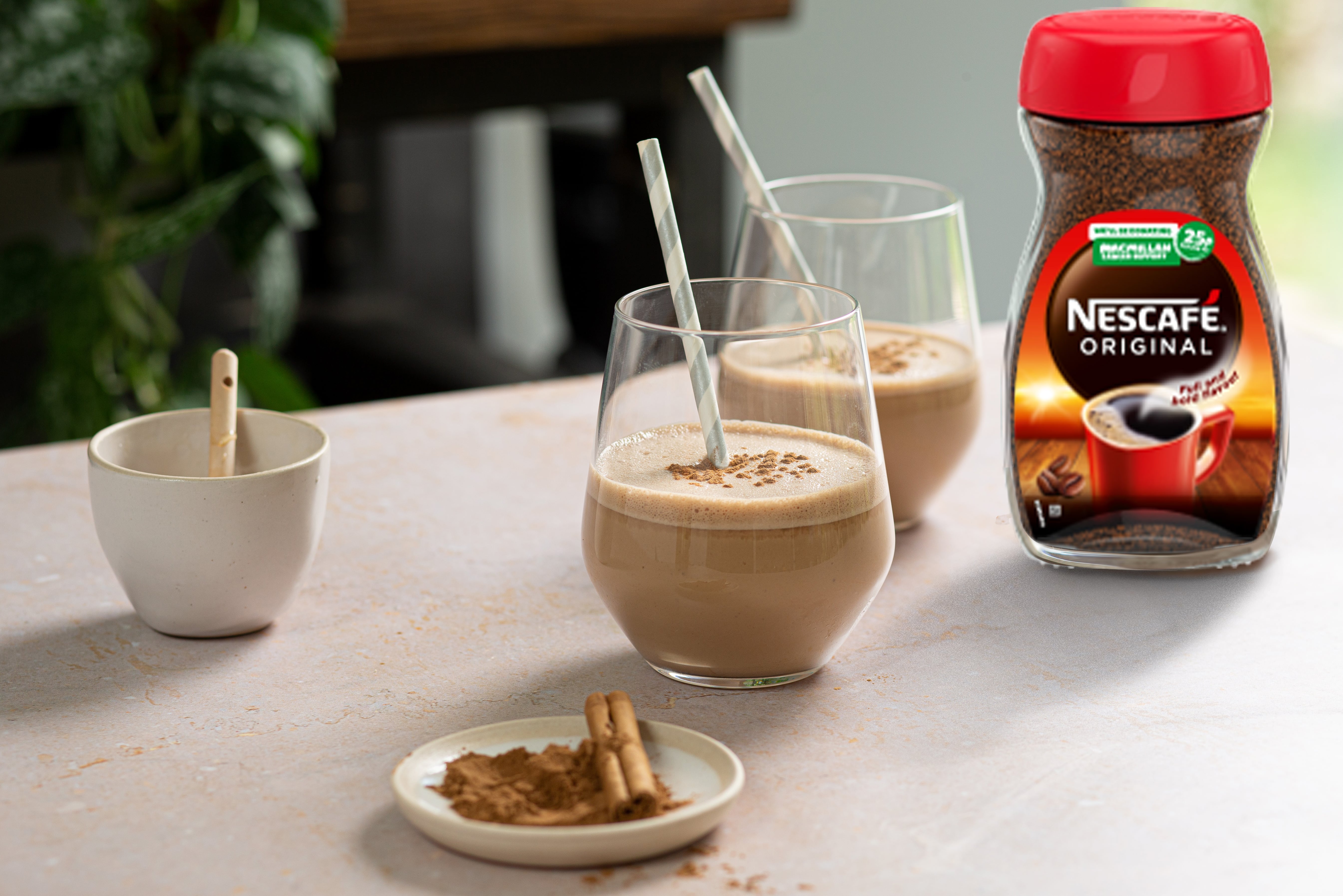 Two glasses of coffee smoothie with a straw. Nescafe original jar is next to the smoothies.